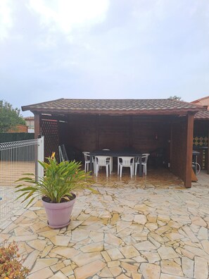 A covered outdoor patio with a stone floor, a table with chairs, and a potted plant. - Less than 10 minutes from the ocean! 5-bedroom family villa with air conditioning, Wi-Fi, and a pool (Claira)