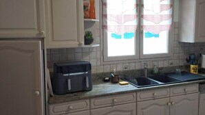 A kitchen with white cabinets, a black coffee maker, a sink, and a window with checkered curtains. - Less than 10 minutes from the ocean! 5-Bedroom Family Villa with Air Conditioning, Wi-Fi, and a Pool (Claira)