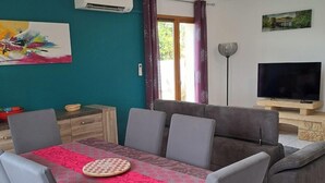 A dining area with a table set for four, a sofa, a TV, and an air conditioning unit on the wall. - Less than 10 minutes from the ocean! 5-Bedroom Family Villa with Air Conditioning, Wi-Fi, and a Pool (Claira)