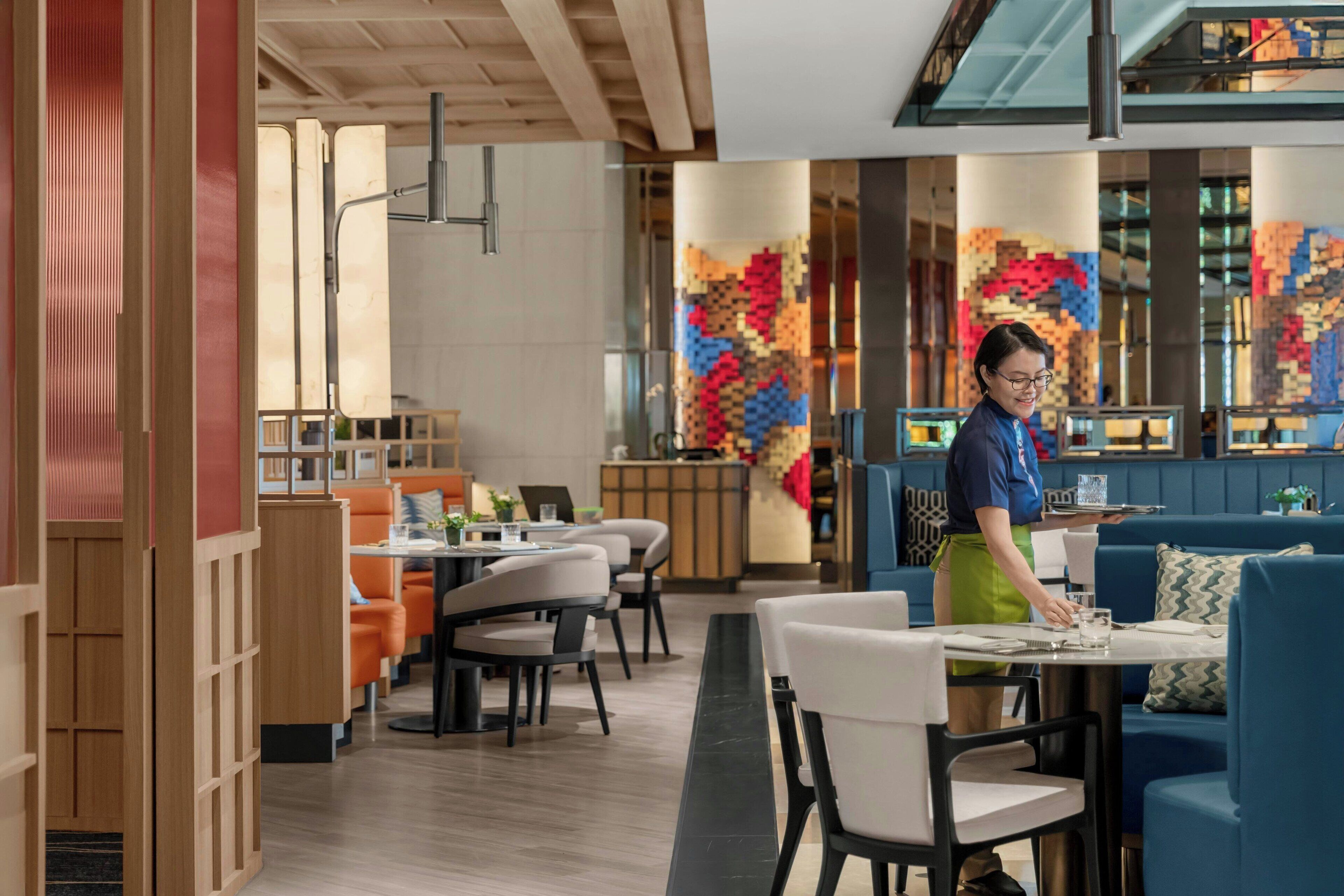 A modern restaurant interior with wooden partitions, seating arrangements, and a colorful wall art installation.