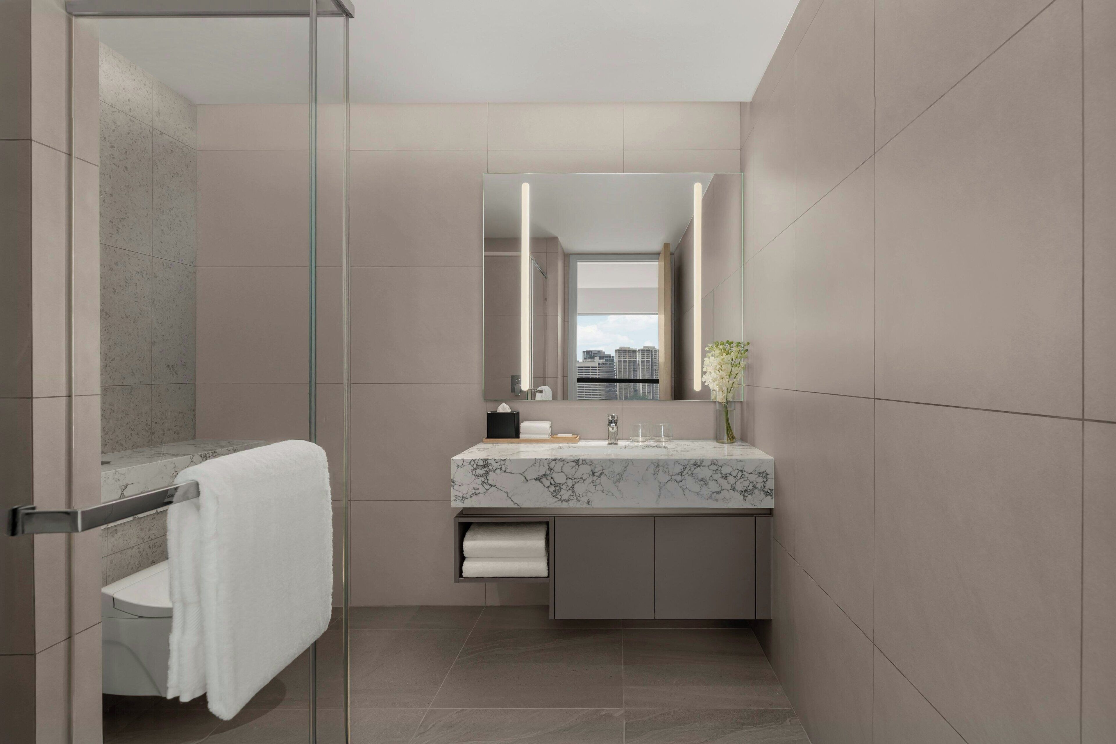 Un baño moderno con cabina de ducha de vidrio, lavamanos de mármol y un espejo grande.