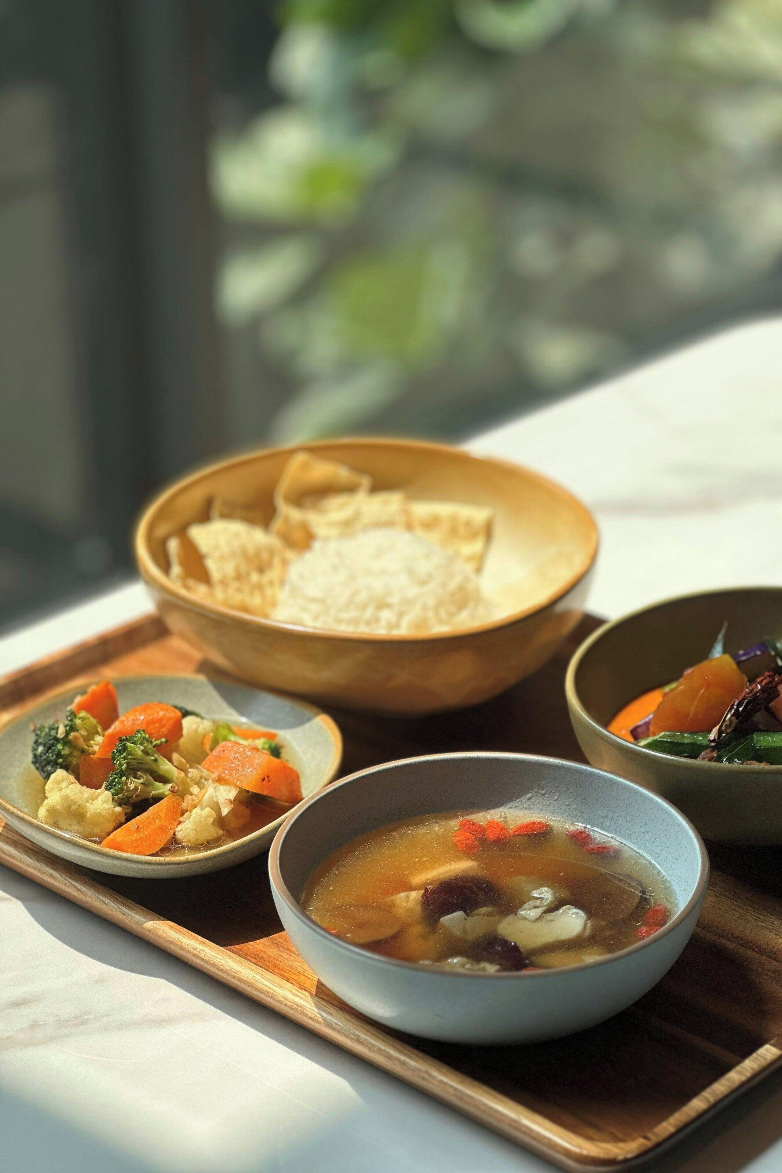 A tray with a bowl of soup, a bowl of rice, and a plate of vegetables.