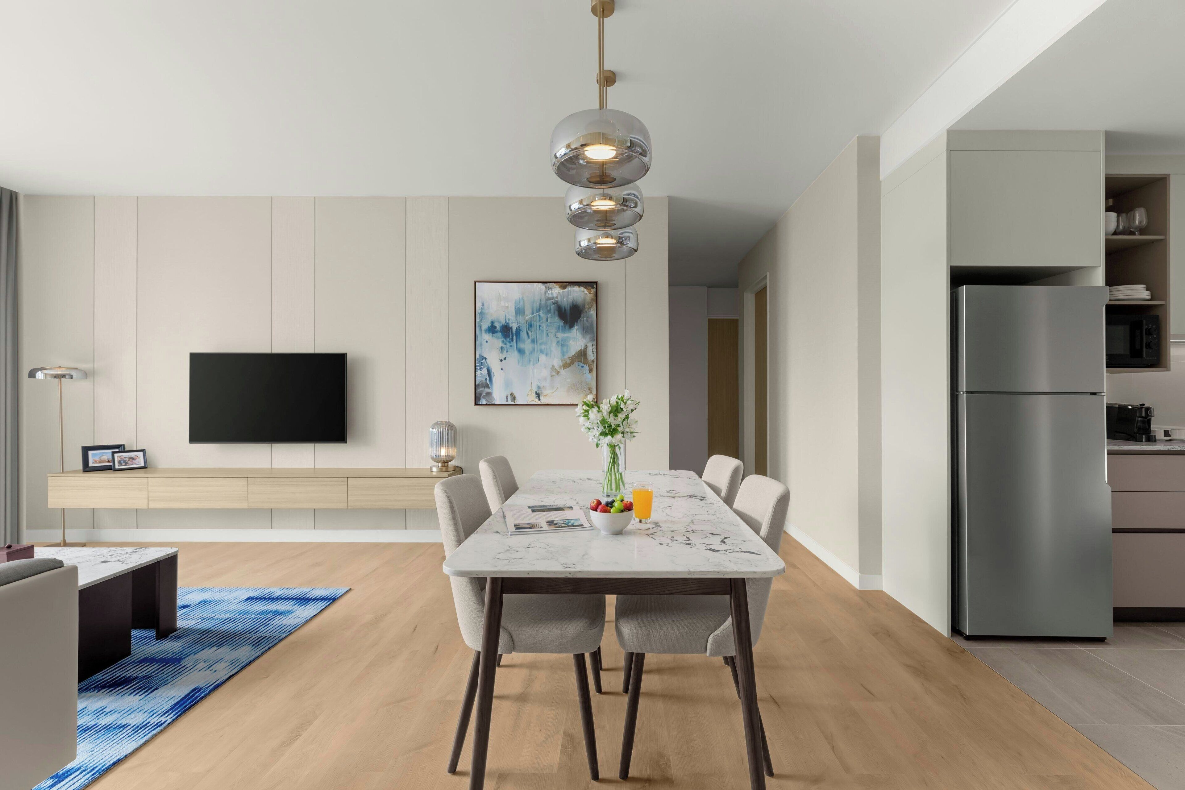 A modern kitchen with a built-in refrigerator, a dining area with a marble table, and a flat-screen TV mounted on the wall.