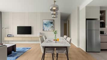 A modern kitchen with a built-in refrigerator, a dining area with a marble table, and a flat-screen TV mounted on the wall.