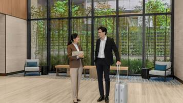A modern indoor space with large windows, a bench, and a person with a suitcase.