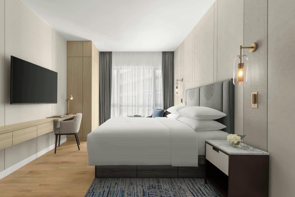 Una habitació d'hotel moderna amb un llit gran, un escriptori, una cadira, un televisor de pantalla plana i una taula de nit amb un vas de flors.