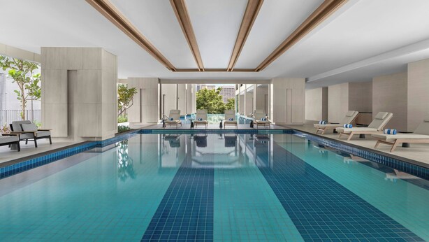 A modern indoor swimming pool with clear blue tiles, lounge chairs, and a view of greenery outside. - Marriott Executive Apartments Kuala Lumpur (Kuala Lumpur)