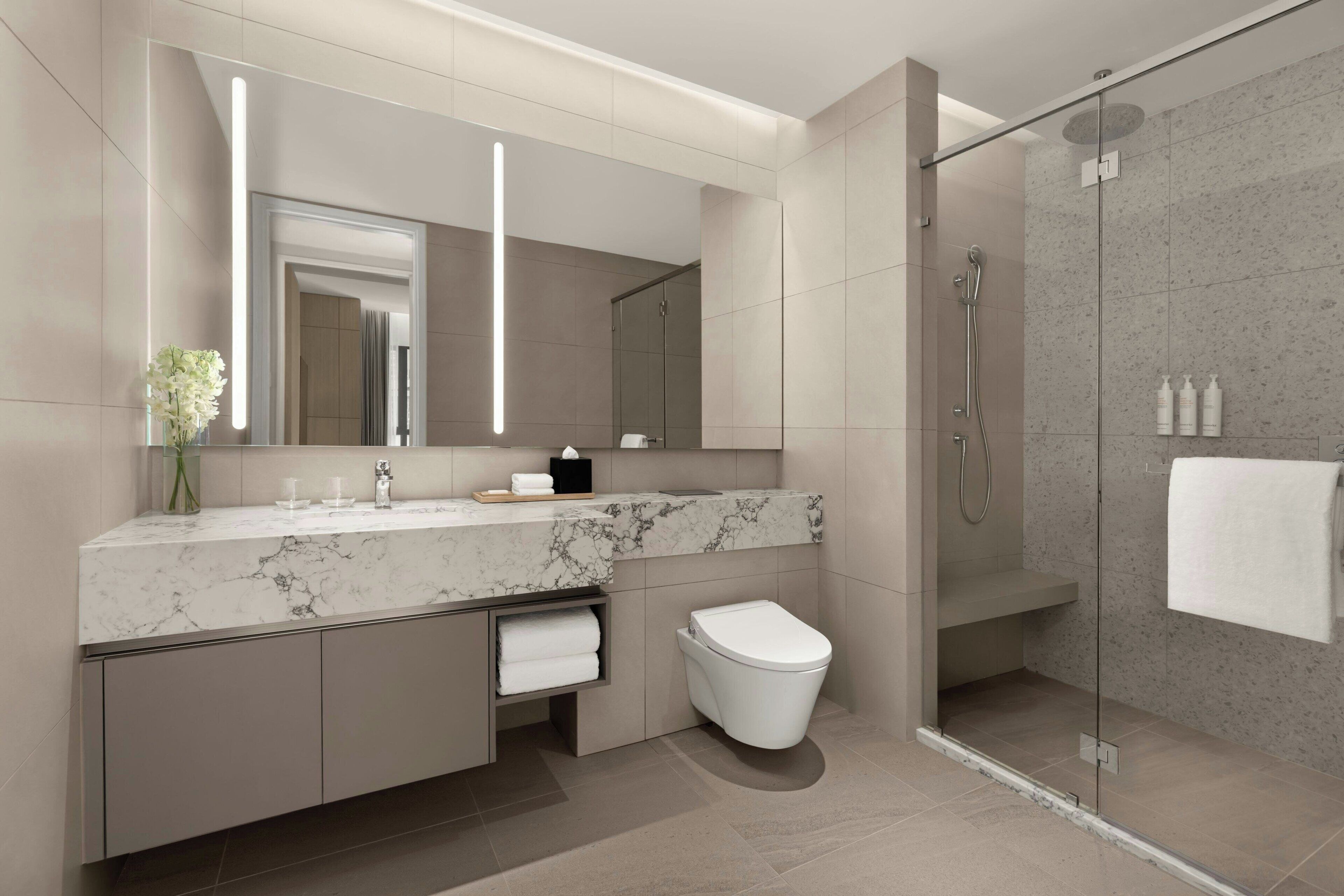 A modern bathroom with a marble sink, a toilet, a glass-enclosed shower, and a large mirror.