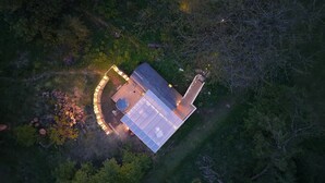 Une vue aérienne d’une maison entourée d’une forêt dense, avec une terrasse et un jacuzzi bien visibles.