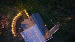 Vue aérienne d’un bâtiment moderne doté d’une grande façade en verre, d’un espace extérieur circulaire aménagé avec des sièges et des éclairages, et d’une terrasse en bois.