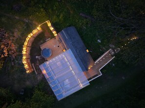 Vue aérienne d’un bâtiment moderne doté d’une grande façade en verre, d’un espace extérieur circulaire aménagé avec des sièges et des éclairages, et d’une terrasse en bois.