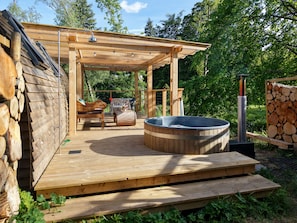 Un área de hidromasaje exterior de madera con una pérgola, un banco de madera, y una mesa con sillas.