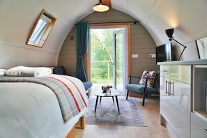 Una habitación acogedora con una cama, una mesita con un florero, una silla y una kitchenette.