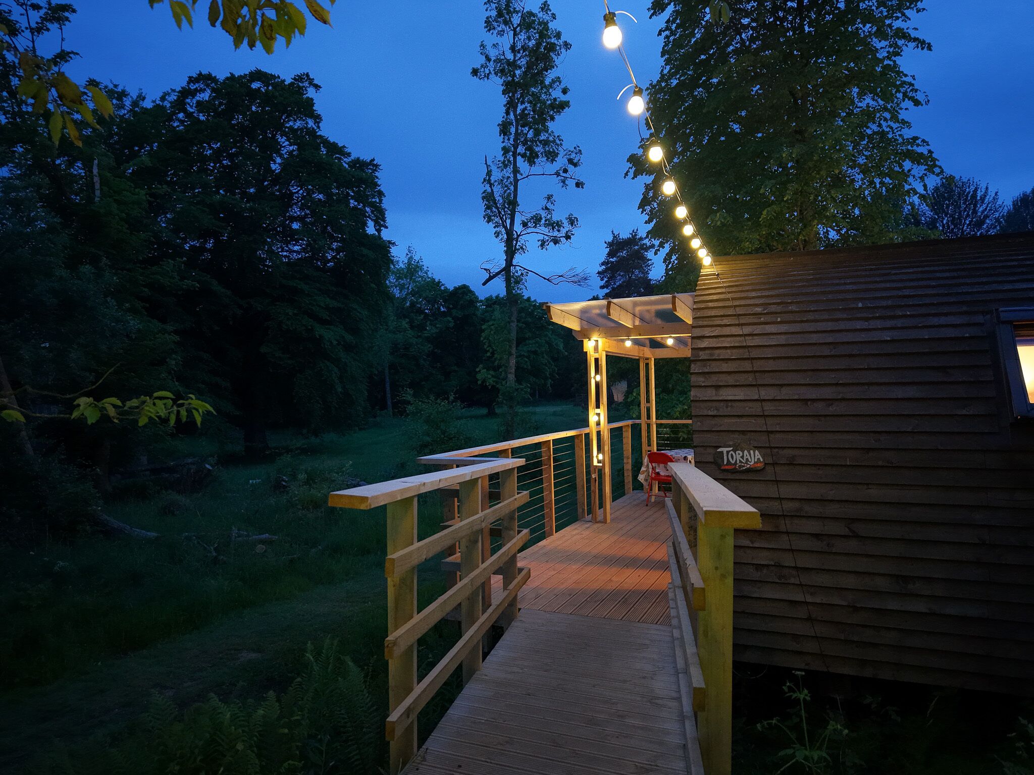 A wooden deck leading to a cabin with a pergola and string lights.