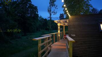 A wooden deck leading to a cabin with a pergola and string lights.