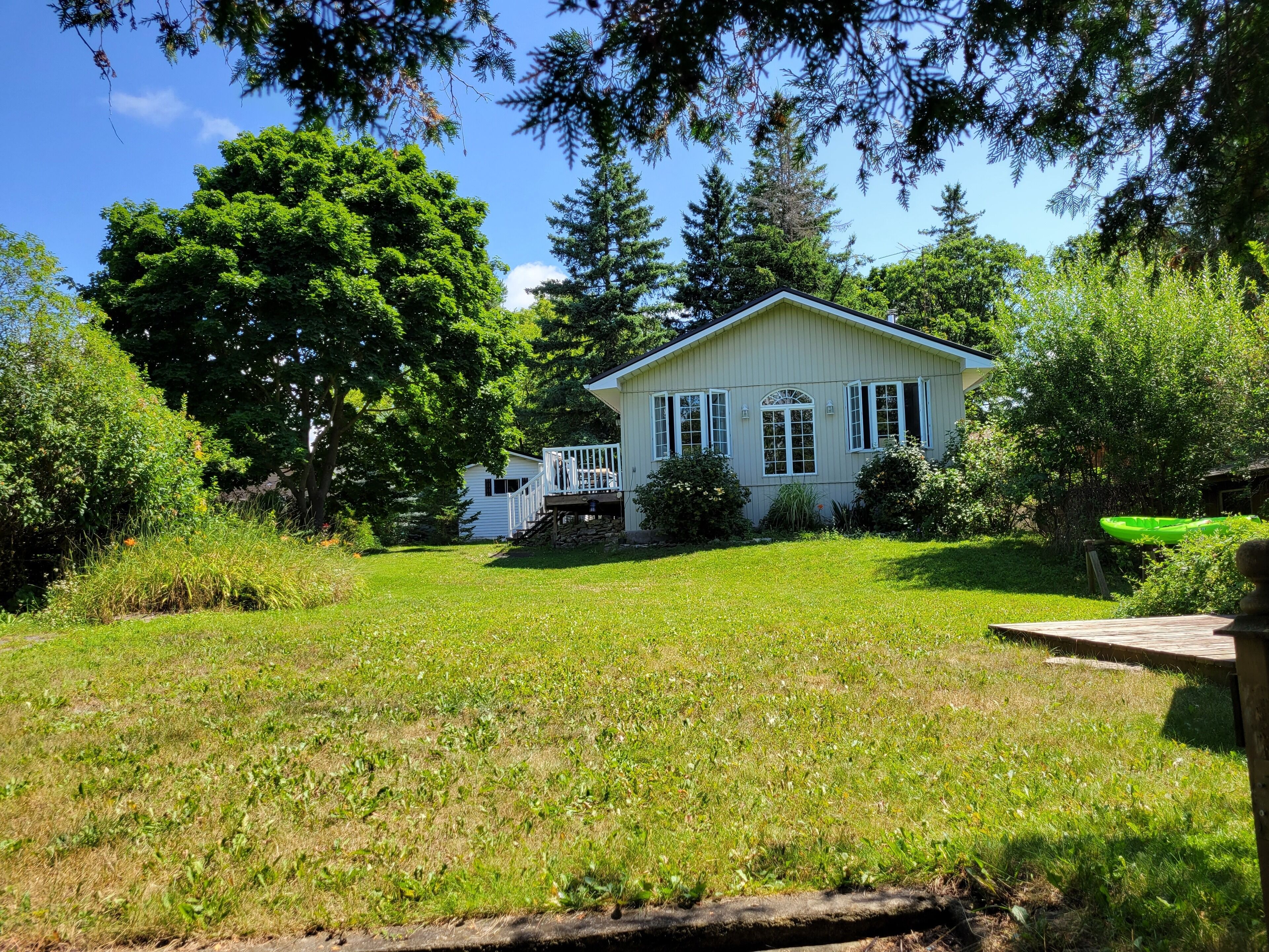 A single-story house with a front porch, surrounded by a well-maintained lawn and dense trees.