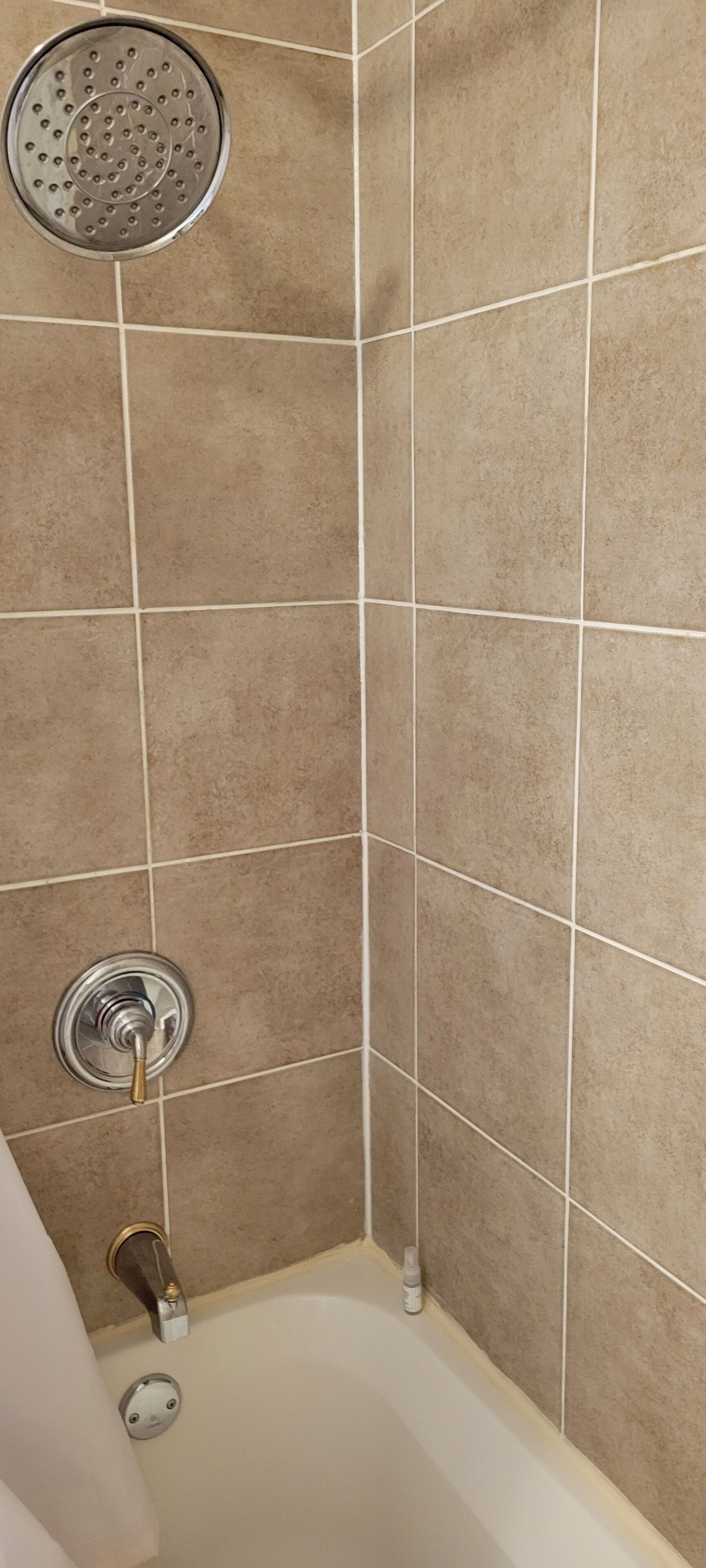 A corner of a bathroom with beige tiles, a showerhead, a faucet, and a bathtub.