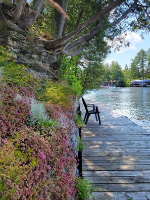 A wooden dock extending into a calm body of water, surrounded by lush greenery and a stone wall.
