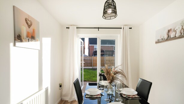 Un comedor con una mesa preparada para cuatro, una silla negra y un florero con plantas secas.