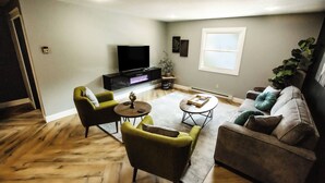Ein Wohnzimmer mit einem Flachbildfernseher, grünen Sesseln, einem braunen Sofa und einem Couchtisch.