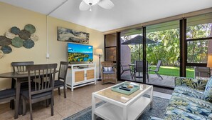 A living room with a dining area, a TV, and a large sliding glass door leading to a patio. - Serene Hawaiian Beachside Bliss (Kihei)