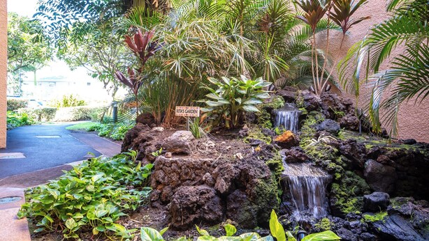 A tropical garden with a waterfall, lush greenery, and a sign indicating a 'Rita's Garden'. - Serene Hawaiian Beachside Bliss (Kihei)