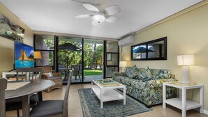 A living room with a sofa, coffee table, TV, and a ceiling fan. - Serene Hawaiian Beachside Bliss (Kihei)