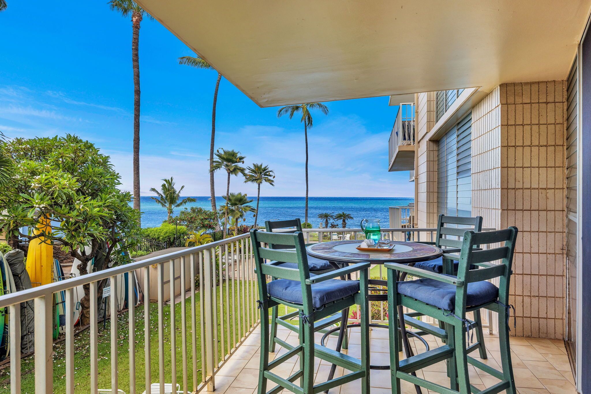 A balcony with a table and chairs, overlooking a beach with palm trees and the ocean.