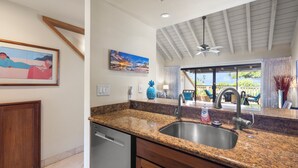A kitchen with granite countertops, a stainless steel sink, wooden cabinets, and a ceiling fan. - Oceanview Poolside Spacious 2-Bed Suite (Kihei)