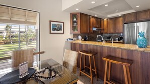 A modern kitchen with wooden cabinets, a stainless steel refrigerator, and a bar area with stools. - Oceanview Poolside Spacious 2-Bed Suite (Kihei)