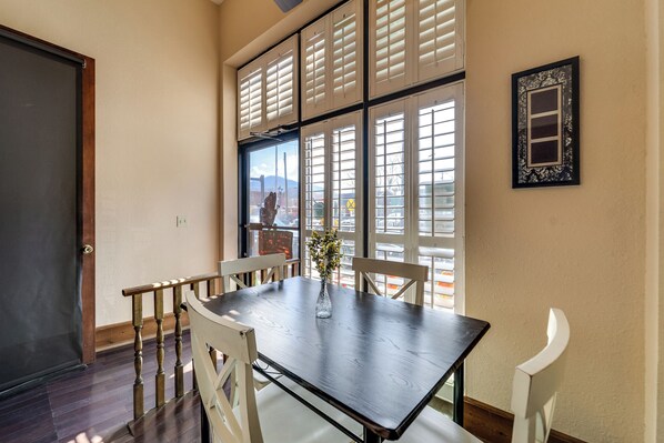 Un comedor con una mesa de madera oscura, sillas blancas y un jarrón con flores.