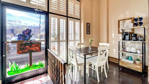 Un comedor con mesa y sillas, una ventana con persianas y una estantería con utensilios de cocina.