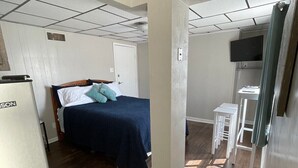 Et lille hotelværelse med en seng, et skrivebord, et fjernsyn og et køleskab.