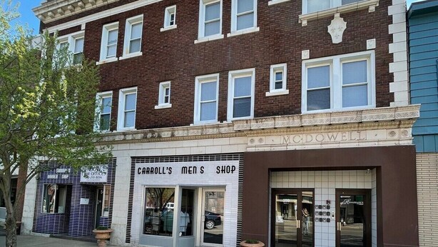 En toetages bygning med et butiksvindue, der viser skiltet "CARROLL'S MEN'S SHOP".