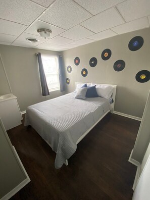 Une chambre à coucher avec un lit, une fenêtre avec des rideaux et un mur décoré de disques vinyle.