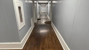 Un long couloir étroit, doté d’un plancher en bois et de murs de couleur gris clair.
