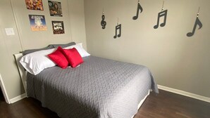 Une chambre à coucher avec un lit, un oreiller rouge, une couverture grise et un mur décoré de notes de musique.