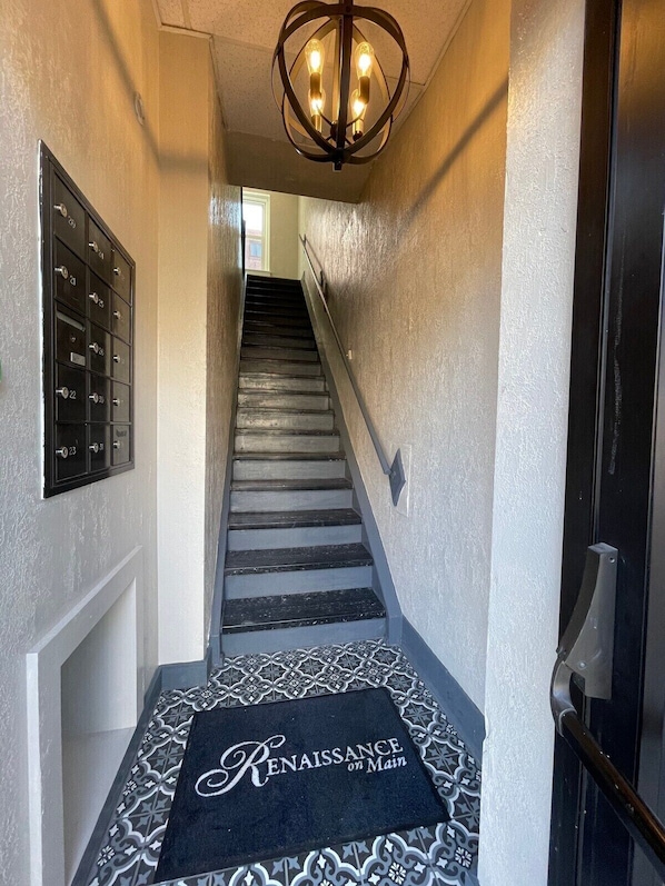 A staircase with a black and white patterned carpet, a metal mail slot on the left, and a chandelier above.