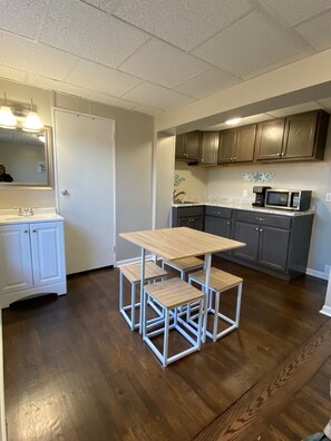 A compact kitchen with a wooden table and matching stools, a microwave, and cabinets.