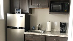 Une cuisine compacte avec des meubles de couleur bois foncé, un réfrigérateur en acier inoxydable, un four à micro-ondes, un évier et une machine à café.