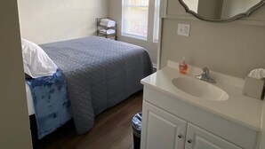 Une chambre d’hôtel avec un lit, une salle de bain comprenant un lavabo et un miroir, et une fenêtre avec des stores.
