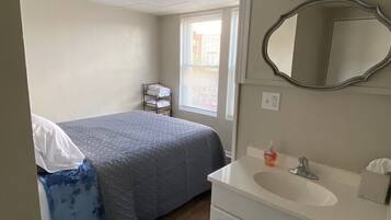 Une chambre d’hôtel avec un lit, une salle de bain comprenant un lavabo et un miroir, et une fenêtre avec des stores.