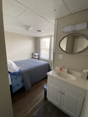 A hotel room with a bed, a bathroom with a sink and mirror, and a window with blinds. - Modern apartment in downtown Coshocton (Coshocton)