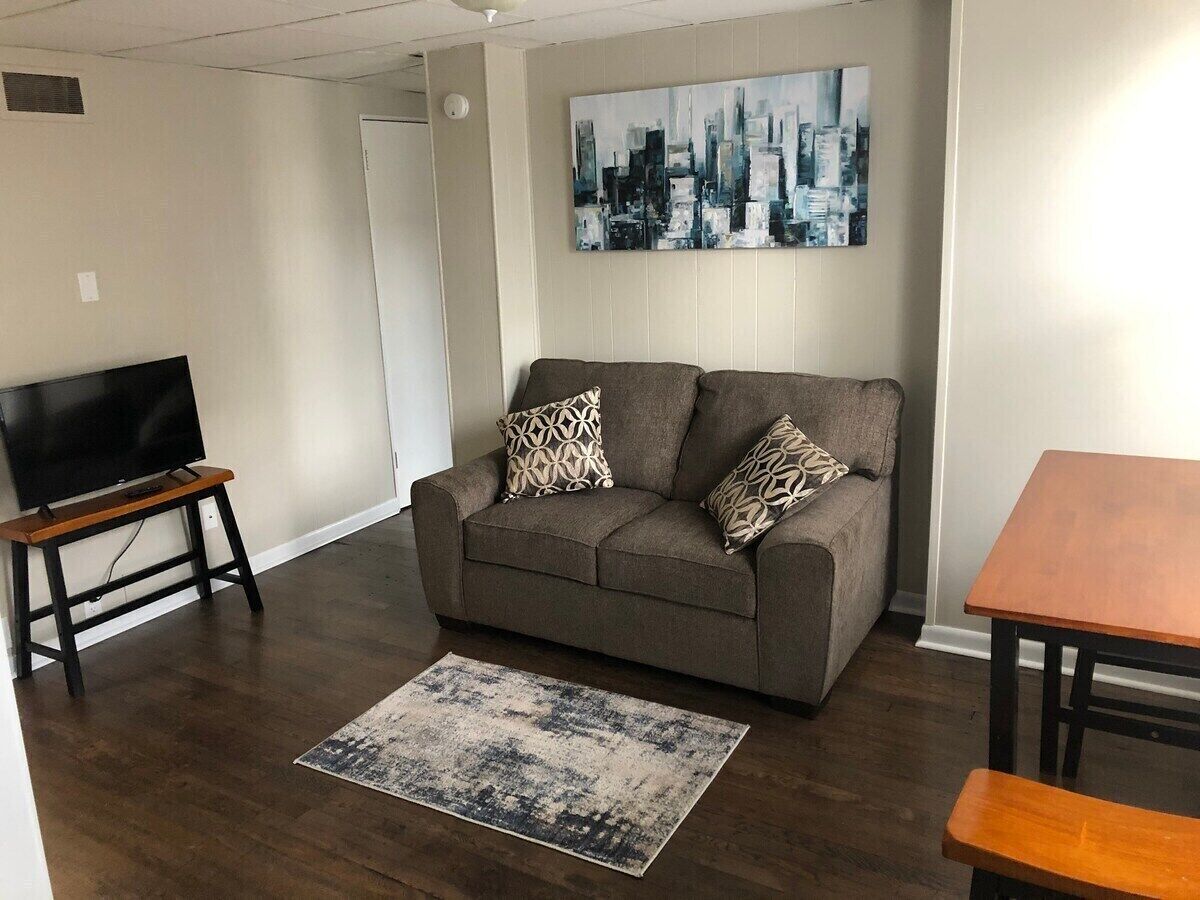 A living room with a sofa, a TV on a stand, a coffee table, and a cityscape painting on the wall.