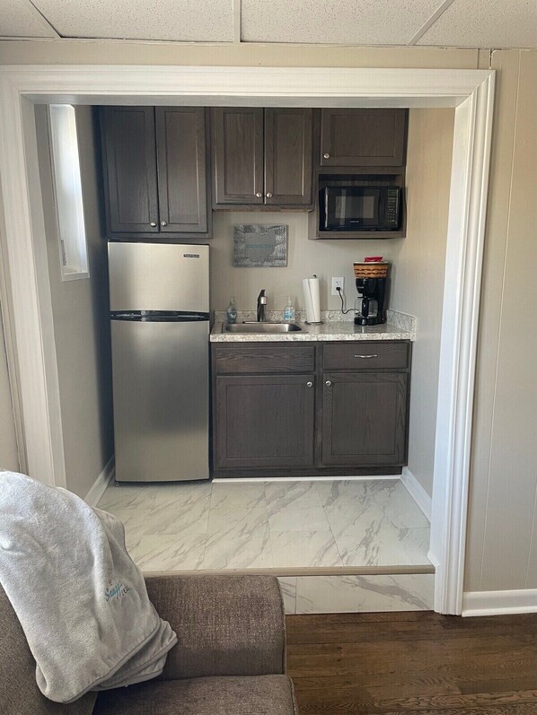 A compact kitchen with dark cabinets, a stainless steel refrigerator, a microwave, and a coffee maker. - Modern apartment in downtown Coshocton (Coshocton)