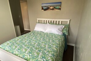A bedroom with a bed, a painting of boats on the wall, and a door leading to another room. - 1 Bedroom Apartment in Downtown Coshocton (30) (Coshocton)