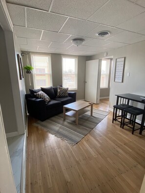 A modern living room with a dark-colored sofa, a wooden coffee table, and a dining area with a small table and benches.