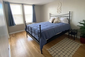 A bedroom with a bed, a window with curtains, a bedside table, and a wall decoration.