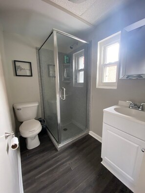 A bathroom with a glass-enclosed shower, a toilet, a sink, and a framed sign on the wall.