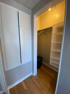 A walk-in closet with a white door, wooden flooring, and a hanging rack.